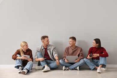 Photo of Group of people using different gadgets near light grey wall indoors. Modern technology