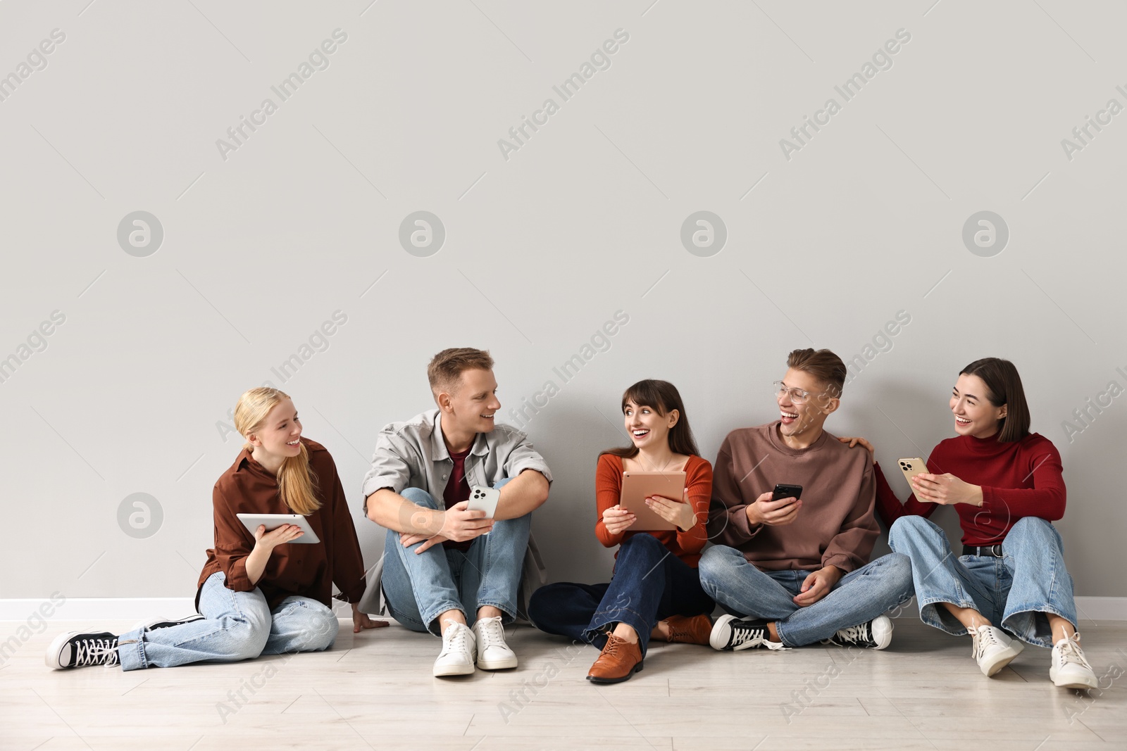 Photo of Group of people using different gadgets near light grey wall indoors. Modern technology