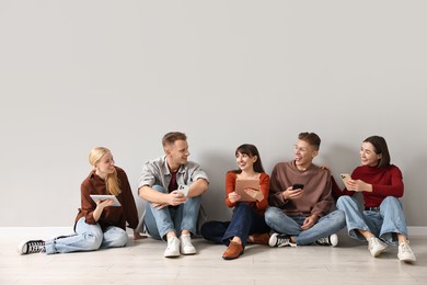 Photo of Group of people using different gadgets near light grey wall indoors. Modern technology