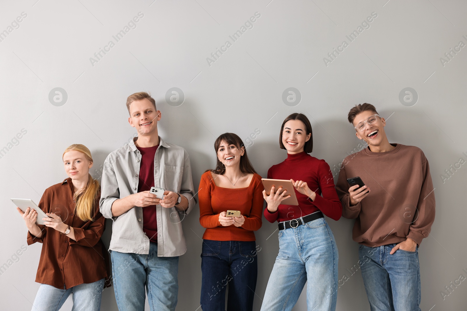 Photo of Group of people using different gadgets near light grey wall indoors. Modern technology