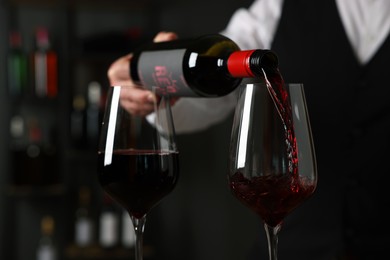 Professional sommelier pouring red wine into glasses indoors, closeup