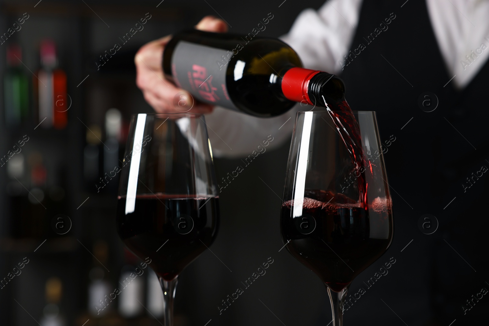 Photo of Professional sommelier pouring red wine into glasses indoors, closeup