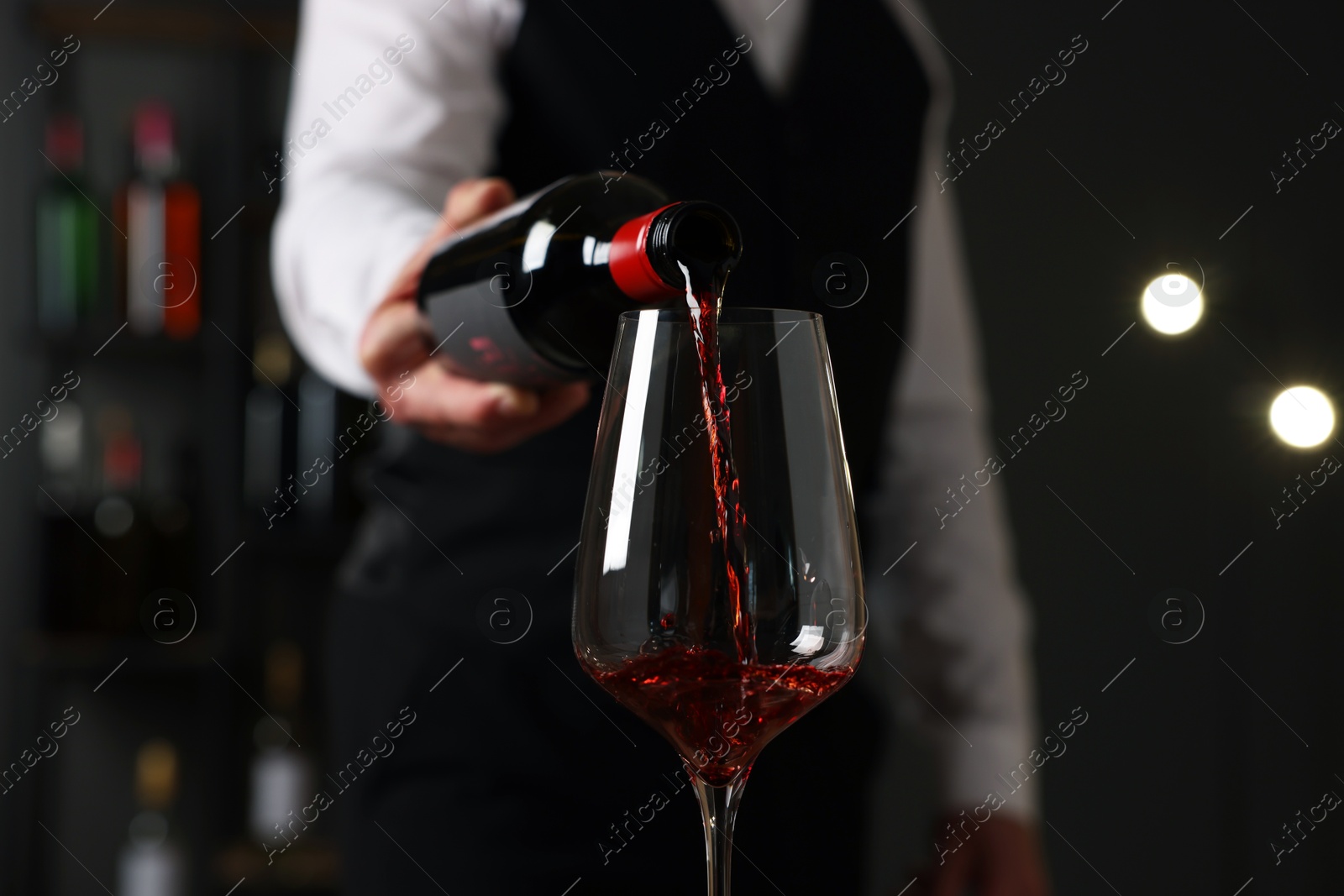 Photo of Professional sommelier pouring red wine into glass indoors, closeup