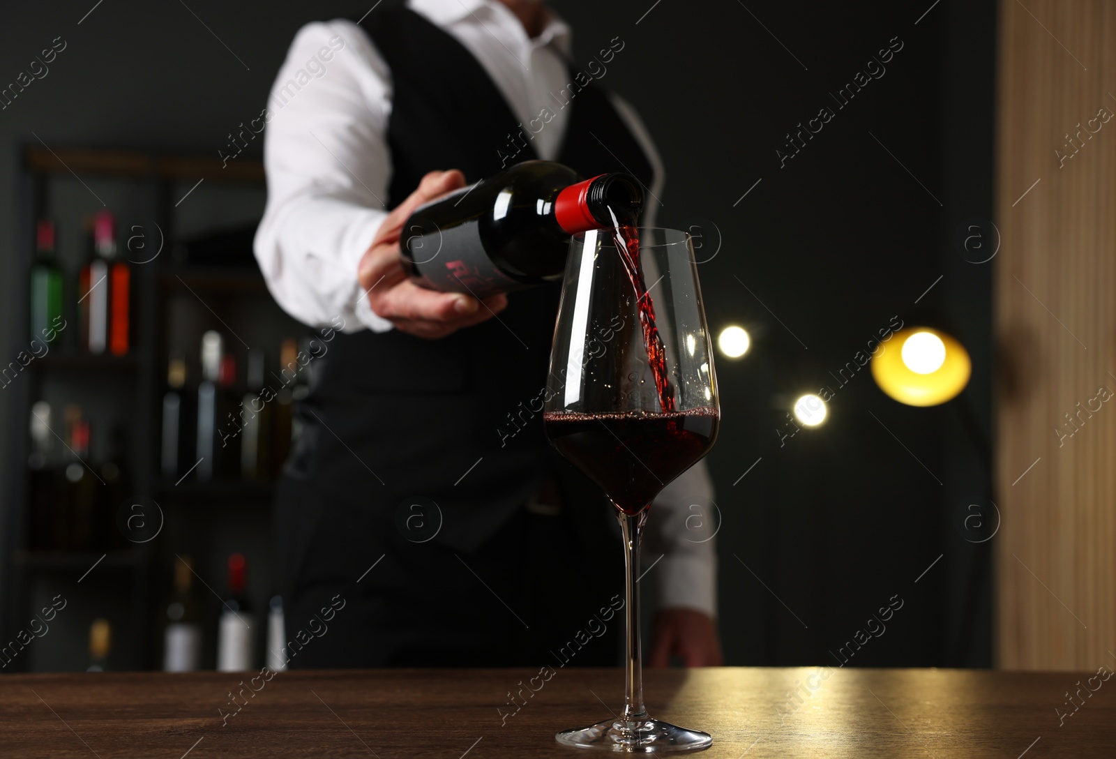 Photo of Professional sommelier pouring red wine into glass at wooden table indoors, closeup