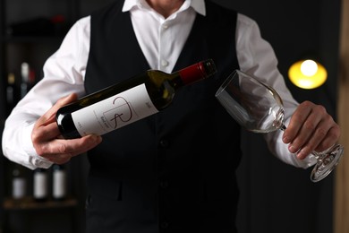 Photo of Professional sommelier pouring red wine into glass indoors, closeup