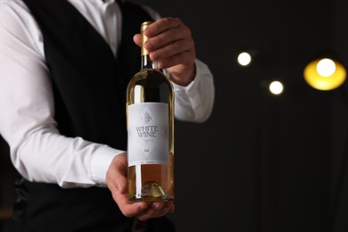 Photo of Professional sommelier holding bottle of white wine indoors, closeup. Space for text