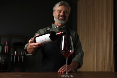 Professional sommelier pouring red wine into glass at wooden table indoors, selective focus