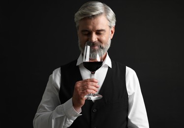 Professional sommelier tasting red wine on black background