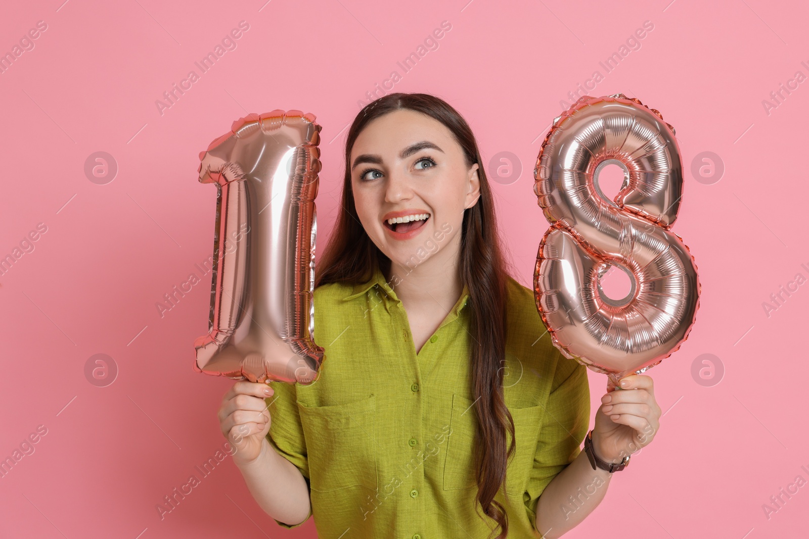 Photo of Coming of age party - 18th birthday. Happy young woman with number shaped balloons on pink background