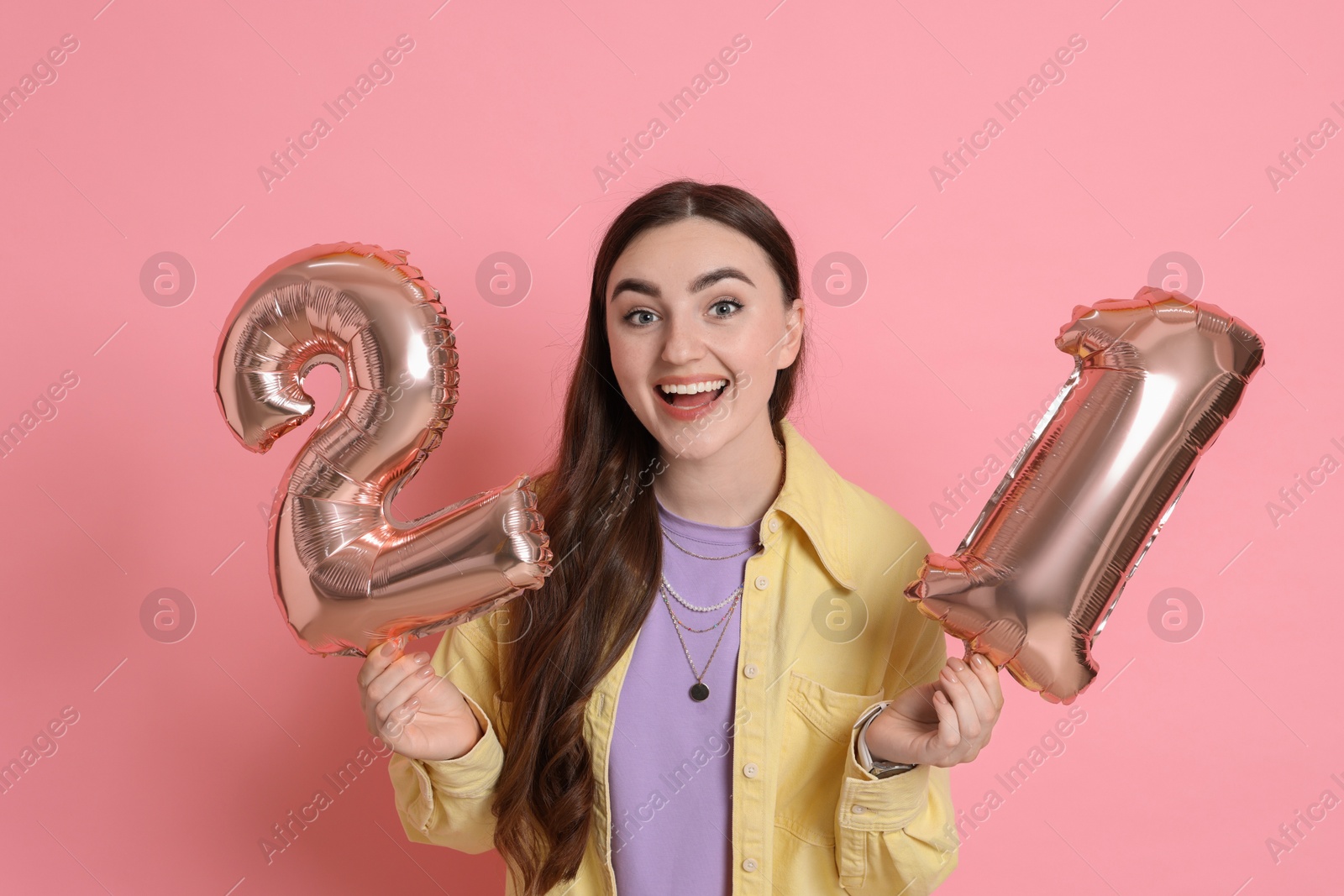 Photo of Coming of age party - 21st birthday. Happy young woman with number shaped balloons on pink background