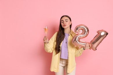 Photo of Coming of age party - 21st birthday. Happy young woman with number shaped balloons and glass of sparkling wine on pink background, space for text