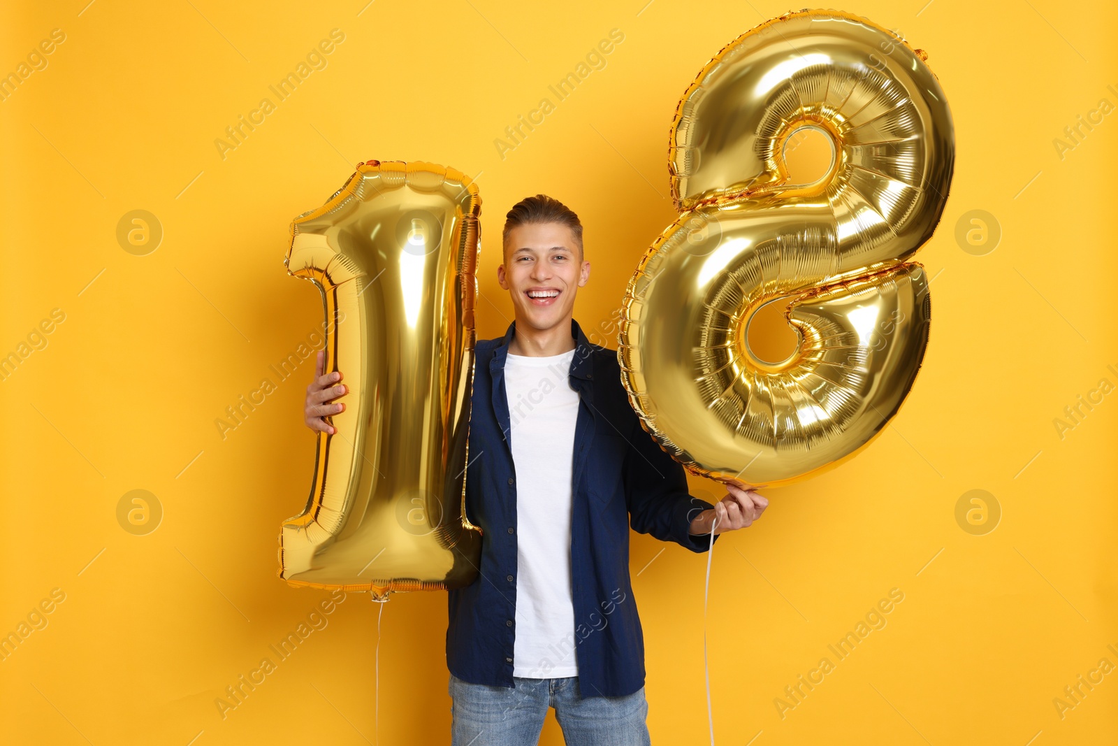 Photo of Coming of age party - 18th birthday. Happy young man with number shaped balloons on yellow background