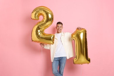 Photo of Coming of age party - 21st birthday. Happy young man with number shaped balloons on pink background