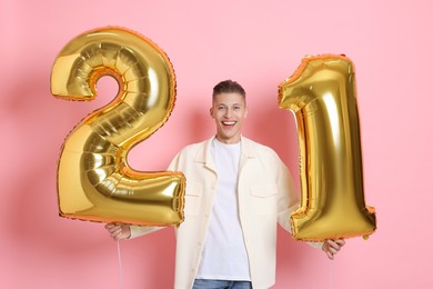 Photo of Coming of age party - 21st birthday. Happy young man with number shaped balloons on pink background