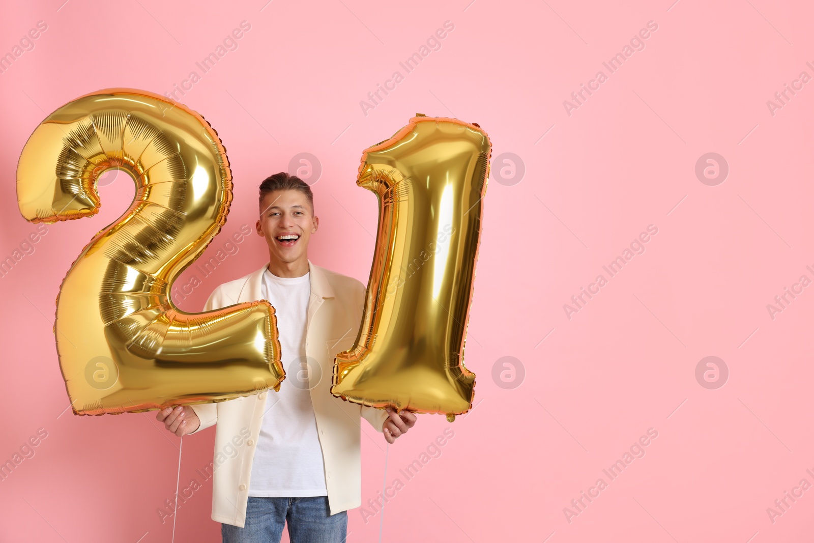 Photo of Coming of age party - 21st birthday. Happy young man with number shaped balloons on pink background, space for text