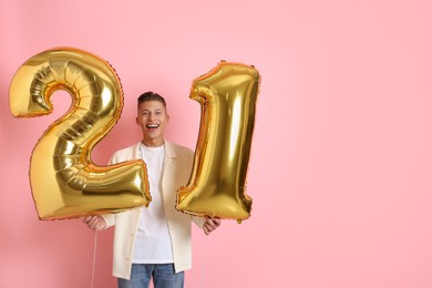 Photo of Coming of age party - 21st birthday. Happy young man with number shaped balloons on pink background, space for text