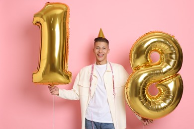 Photo of Coming of age party - 18th birthday. Happy young man with number shaped balloons and hat on pink background