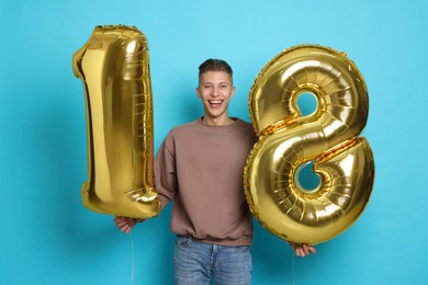 Photo of Coming of age party - 18th birthday. Happy young man with number shaped balloons on light blue background