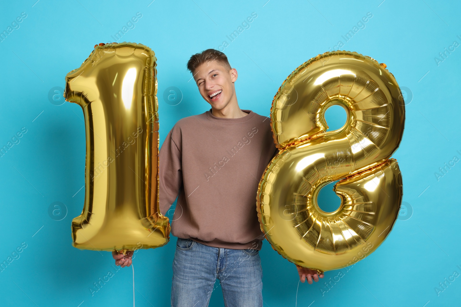 Photo of Coming of age party - 18th birthday. Happy young man with number shaped balloons on light blue background