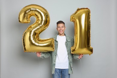 Photo of Coming of age party - 21st birthday. Happy young man with number shaped balloons on light grey background