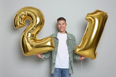 Photo of Coming of age party - 21st birthday. Happy young man with number shaped balloons on light grey background