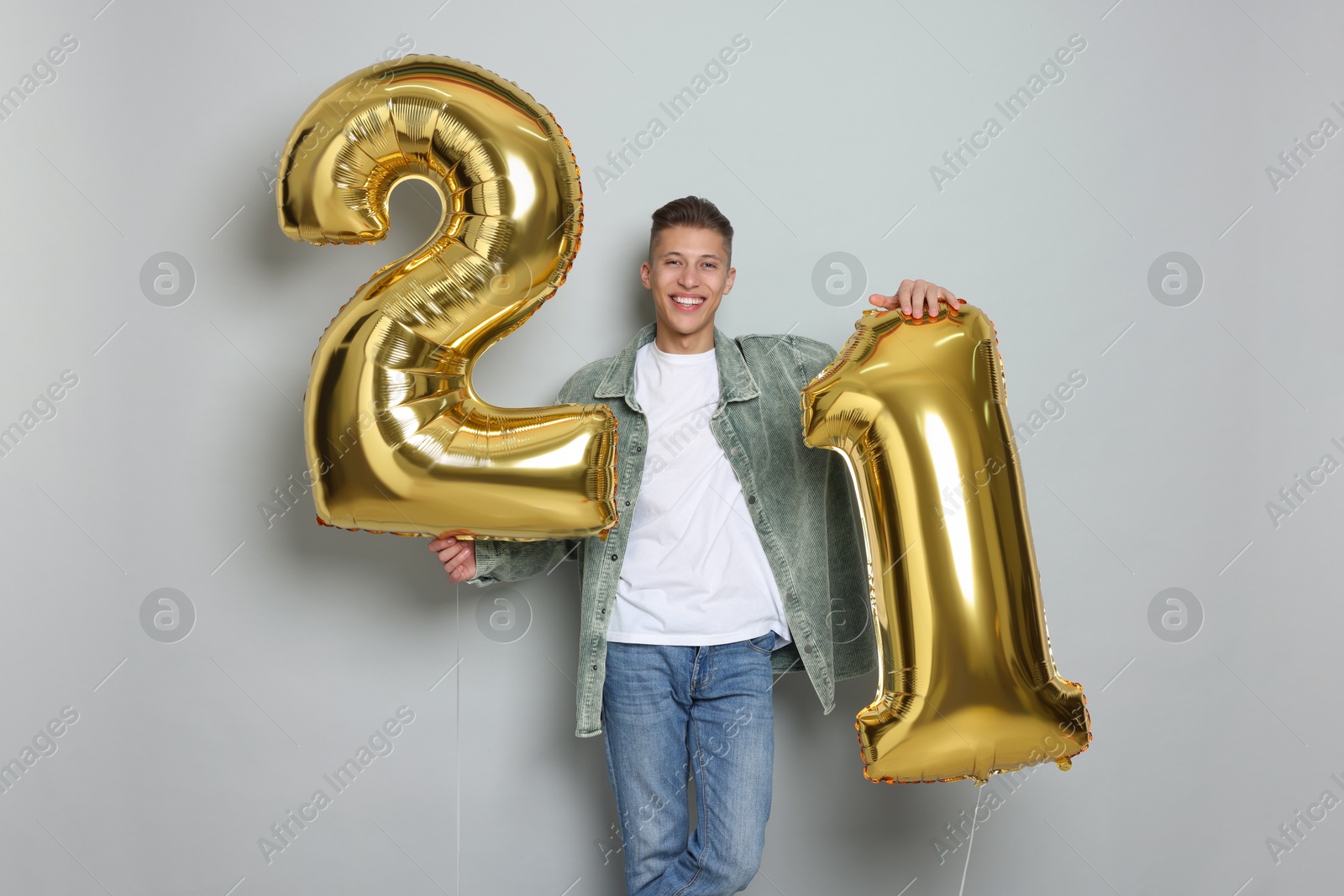 Photo of Coming of age party - 21st birthday. Happy young man with number shaped balloons on light grey background