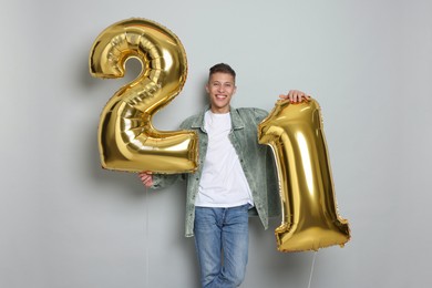 Photo of Coming of age party - 21st birthday. Happy young man with number shaped balloons on light grey background