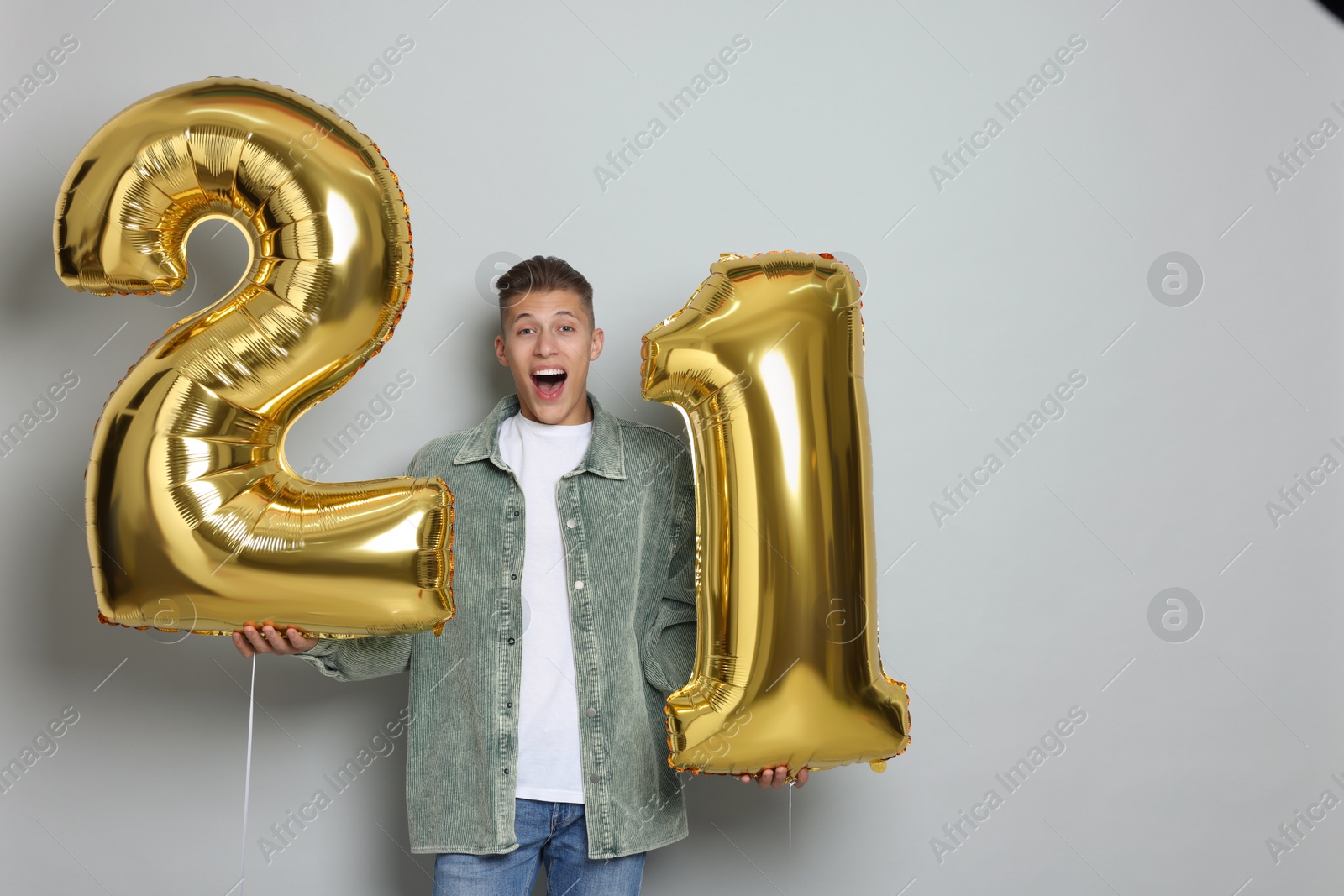 Photo of Coming of age party - 21st birthday. Happy young man with number shaped balloons on light grey background, space for text