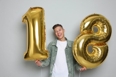 Photo of Coming of age party - 18th birthday. Happy young man with number shaped balloons on light grey background