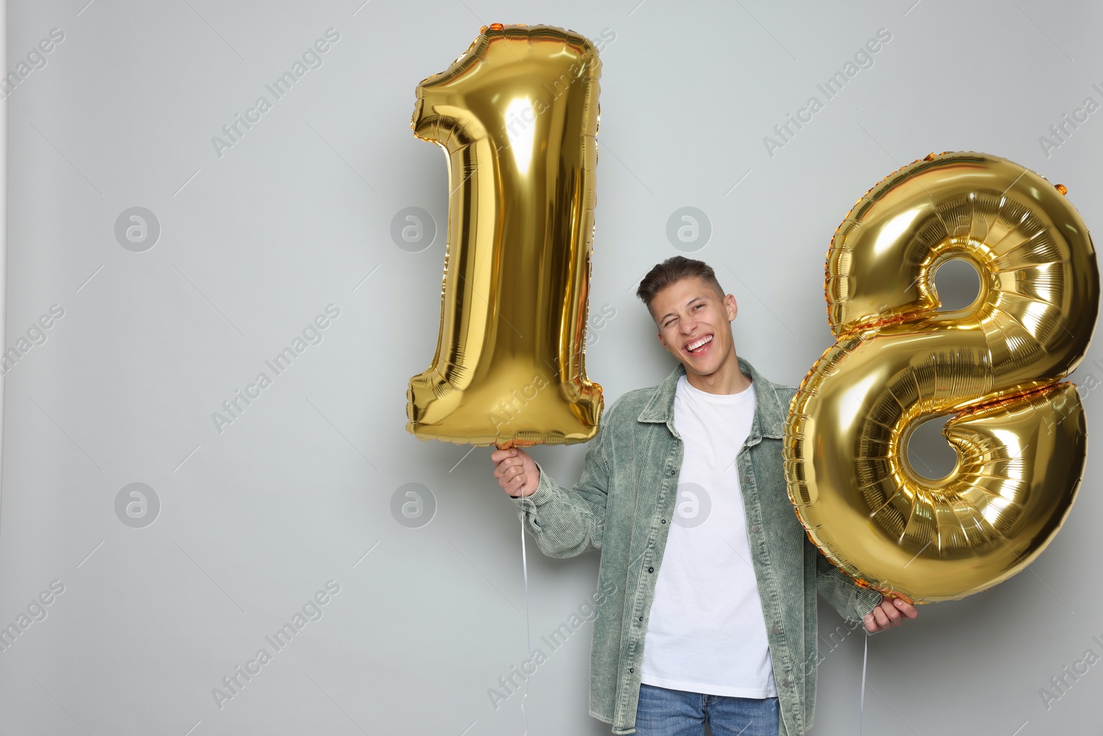 Photo of Coming of age party - 18th birthday. Happy young man with number shaped balloons on light grey background, space for text