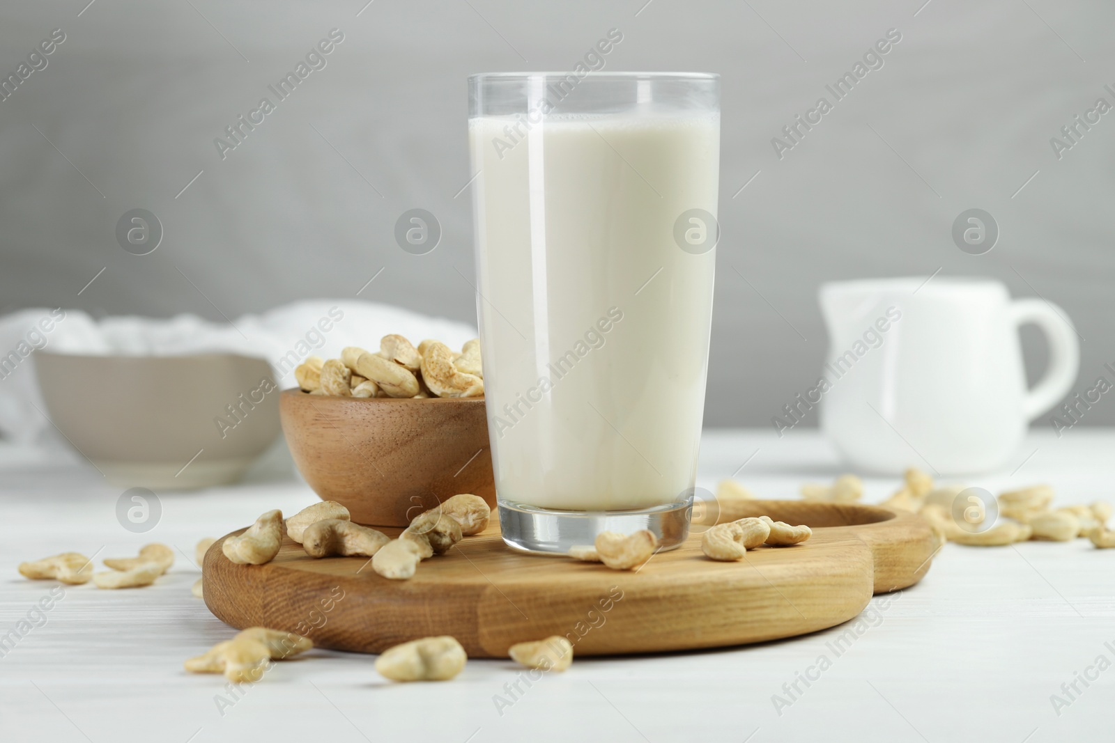 Photo of Fresh cashew milk in glass and nuts on white wooden table