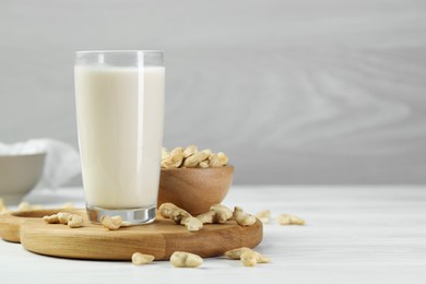 Photo of Fresh cashew milk in glass and nuts on white wooden table, space for text