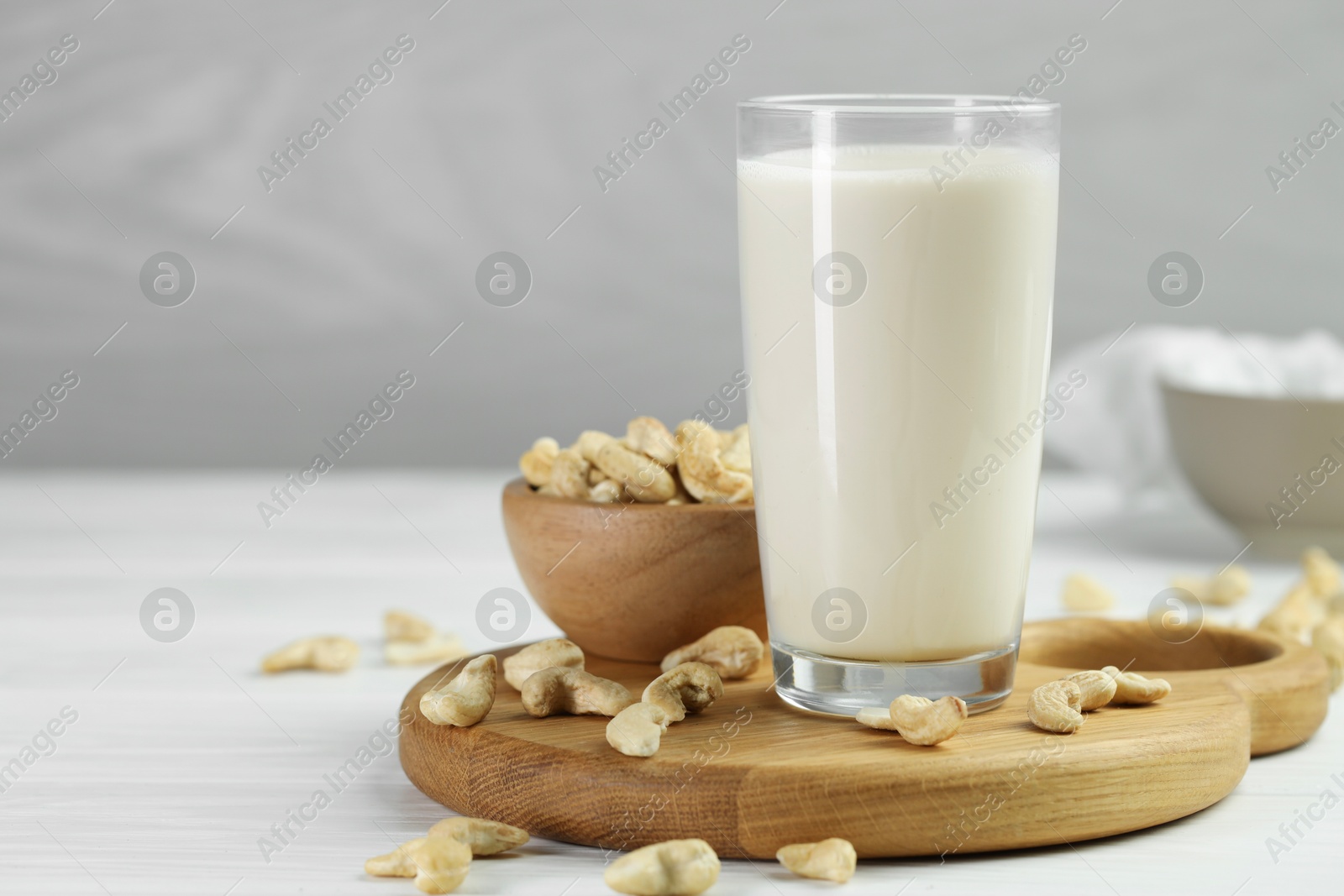 Photo of Fresh cashew milk in glass and nuts on white wooden table, closeup. Space for text