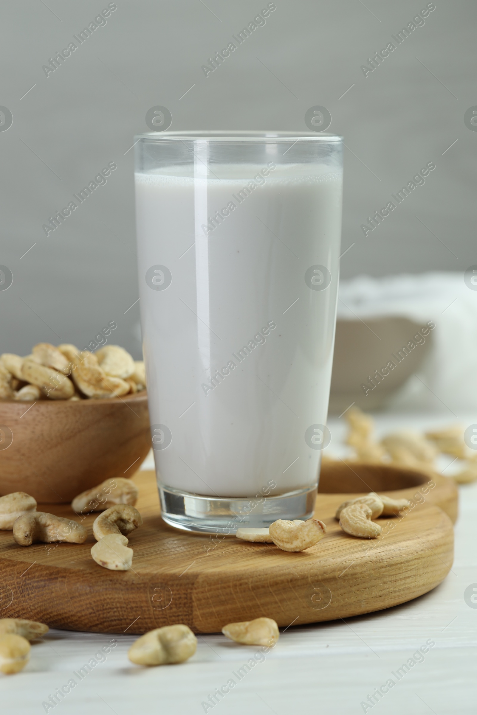 Photo of Fresh cashew milk in glass and nuts on white wooden table, closeup