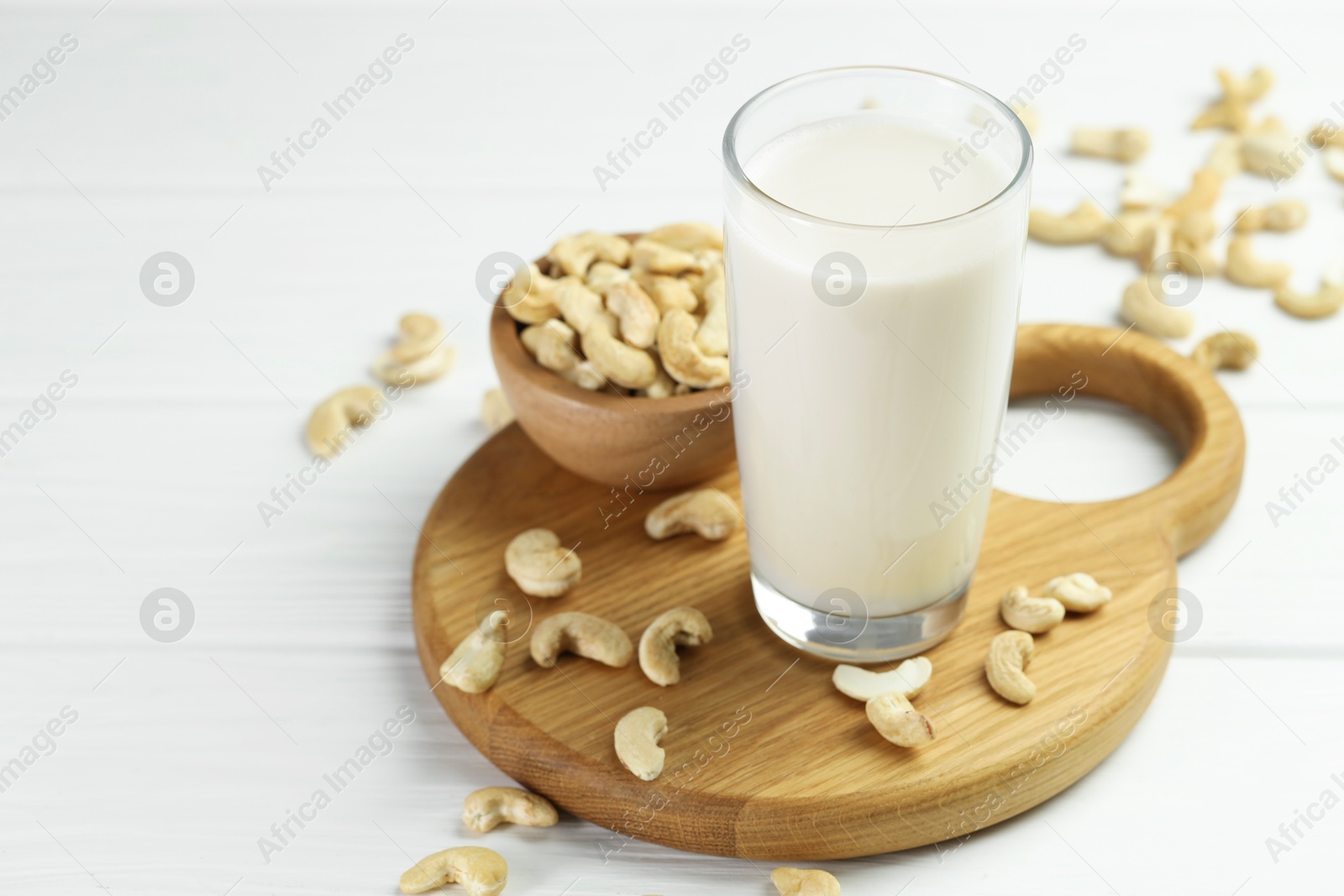 Photo of Fresh cashew milk in glass and nuts on white wooden table, closeup. Space for text