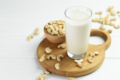 Photo of Fresh cashew milk in glass and nuts on white wooden table, closeup. Space for text