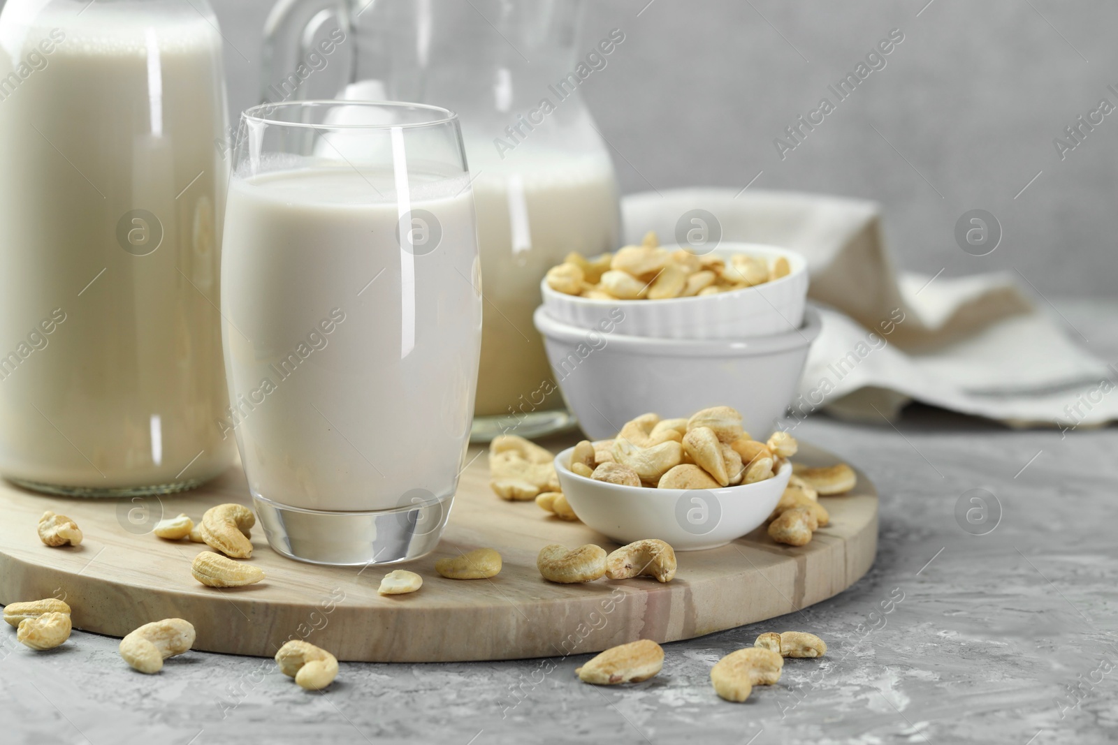 Photo of Glassware with fresh cashew milk and nuts on grey table, closeup