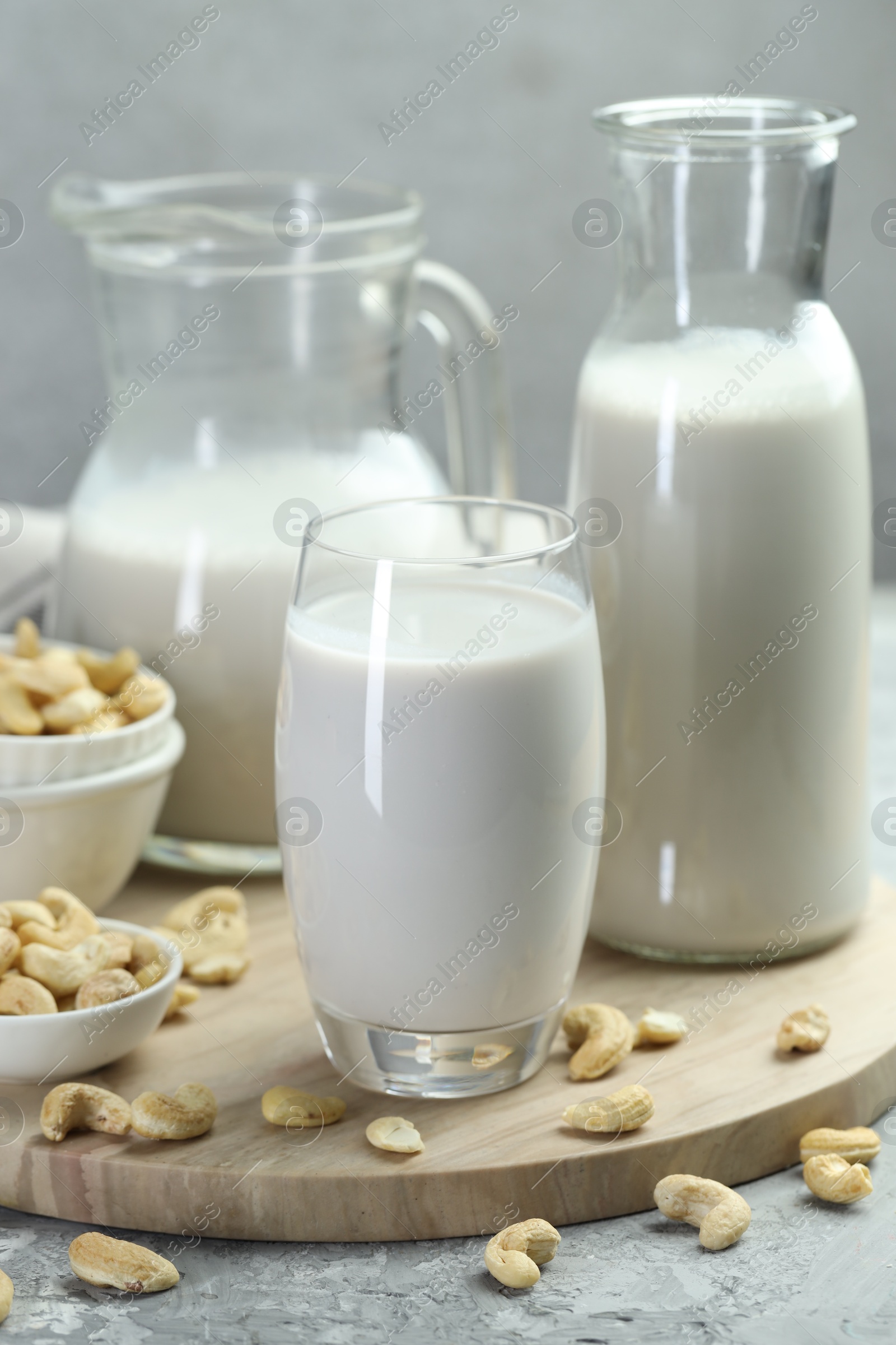 Photo of Glassware with fresh cashew milk and nuts on grey table, closeup