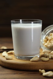 Photo of Fresh cashew milk in glass and nuts on wooden table, closeup