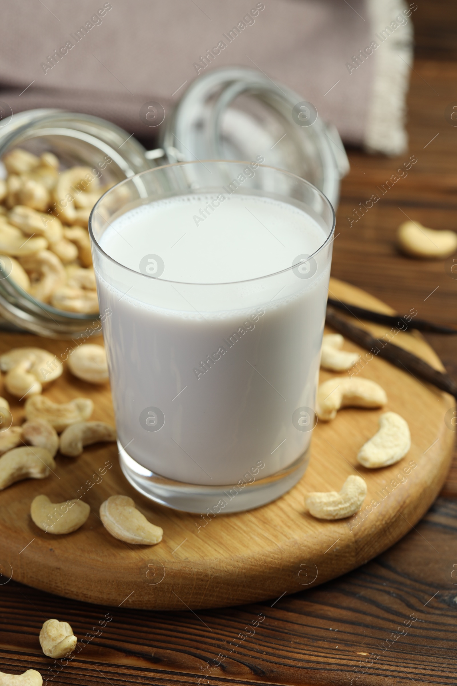 Photo of Fresh cashew milk in glass, nuts and vanilla pods on wooden table, closeup