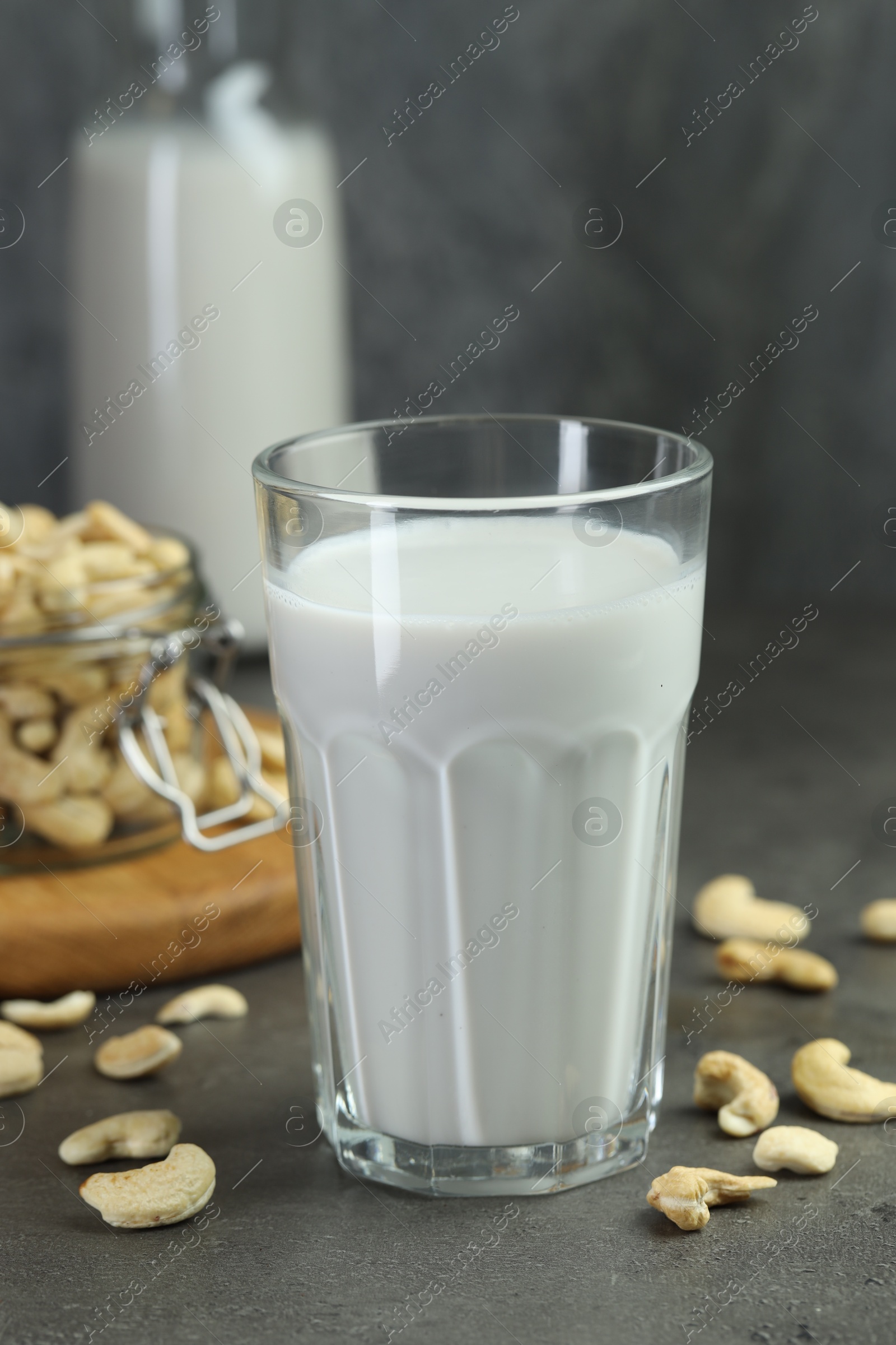 Photo of Fresh cashew milk in glass and nuts on grey table, closeup