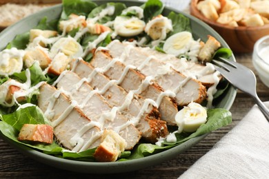 Photo of Delicious Caesar salad with chicken on wooden table, closeup