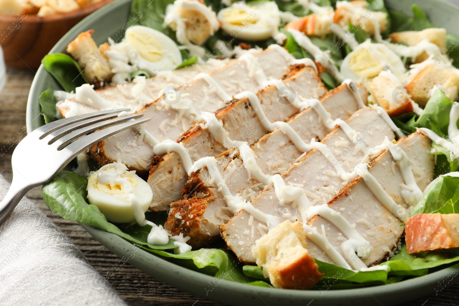 Photo of Delicious Caesar salad with chicken on wooden table, closeup