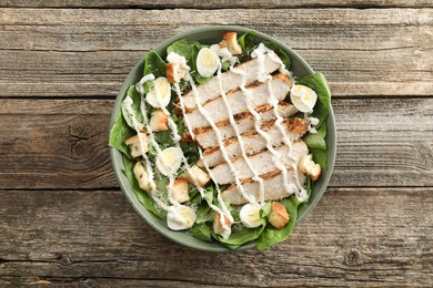 Photo of Delicious Caesar salad with chicken on wooden table, top view