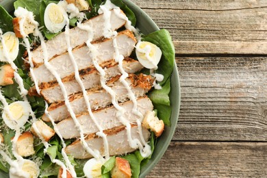 Photo of Delicious Caesar salad with chicken on wooden table, top view. Space for text