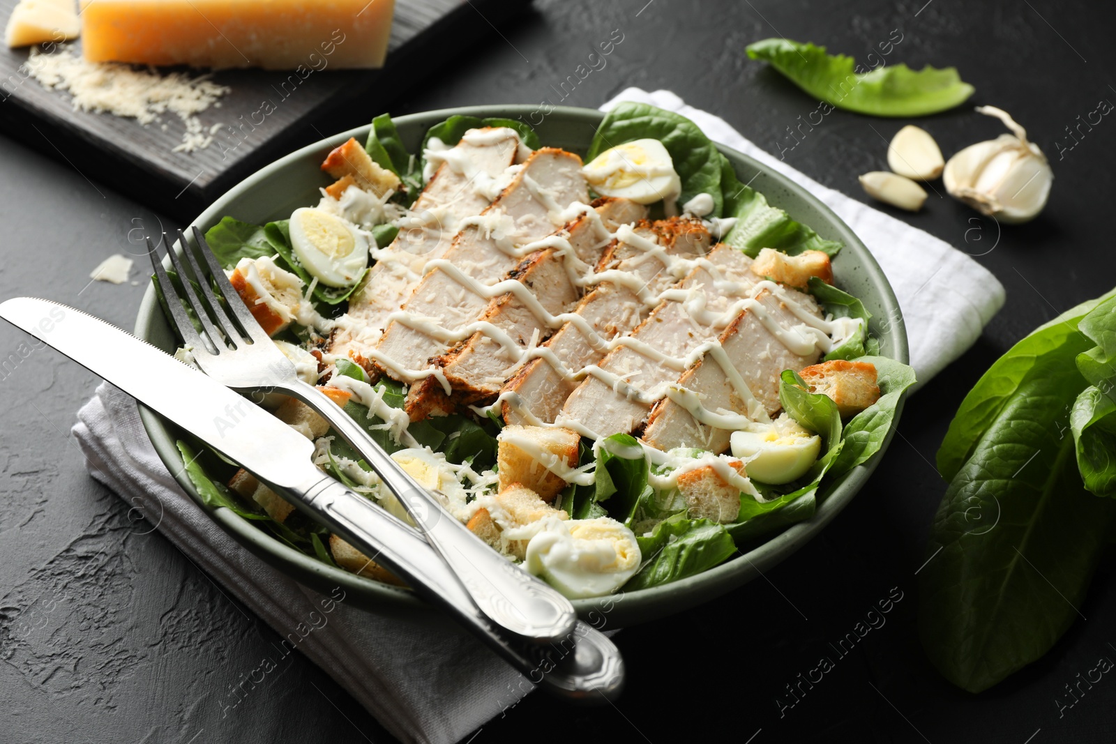 Photo of Delicious Caesar salad with chicken on black textured table, closeup