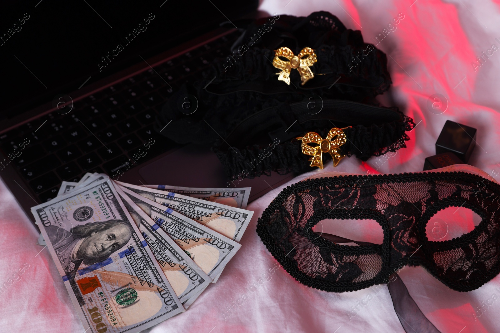 Photo of Prostitution and virtual sex. Laptop, dollar banknotes and mask on linens