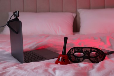 Photo of Prostitution and virtual sex. Laptop with web camera, bell and mask on bed