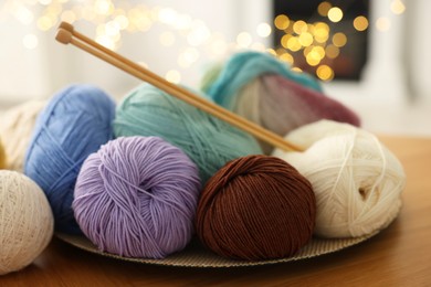 Photo of Colorful yarns and knitting needles on wooden table against blurred lights, closeup