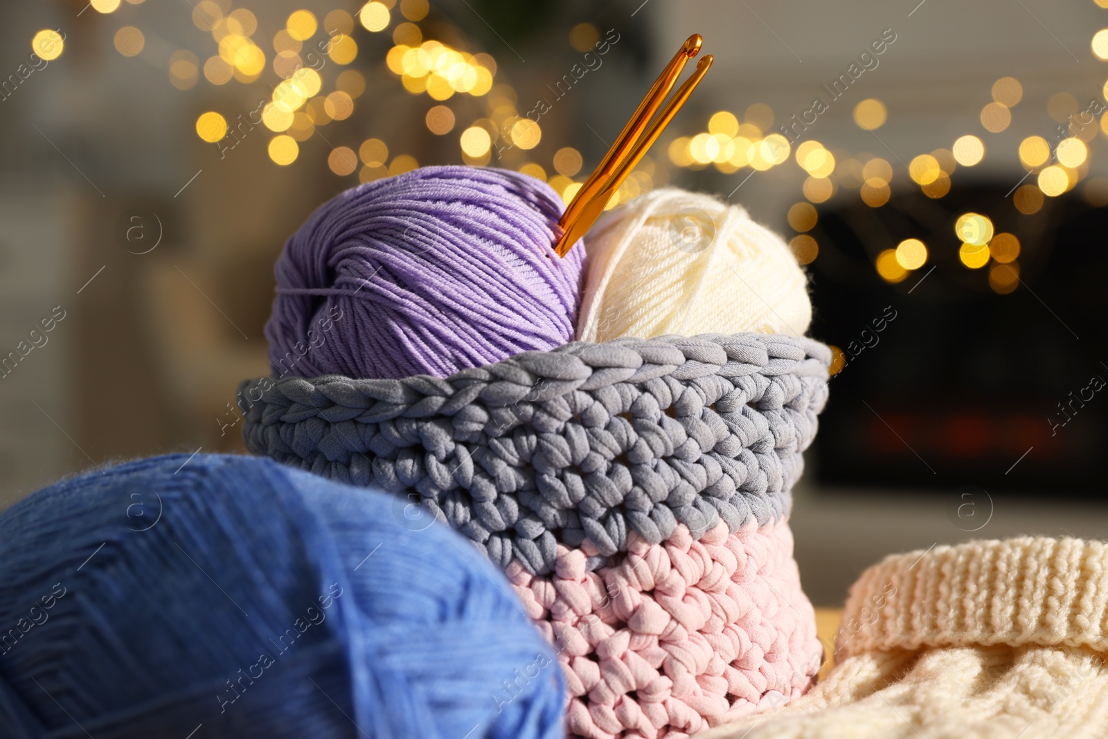 Photo of Basket with colorful yarns and crochet hooks against blurred lights, closeup